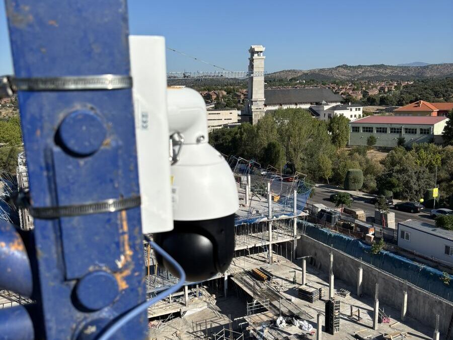 Dome camera clamped to a blue crane mast above a concrete structure